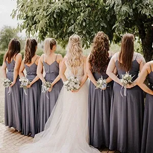 Braut steht mit all ihren Brautjungfern im Arm in einer Reihe und sind von hinten fotografiert.