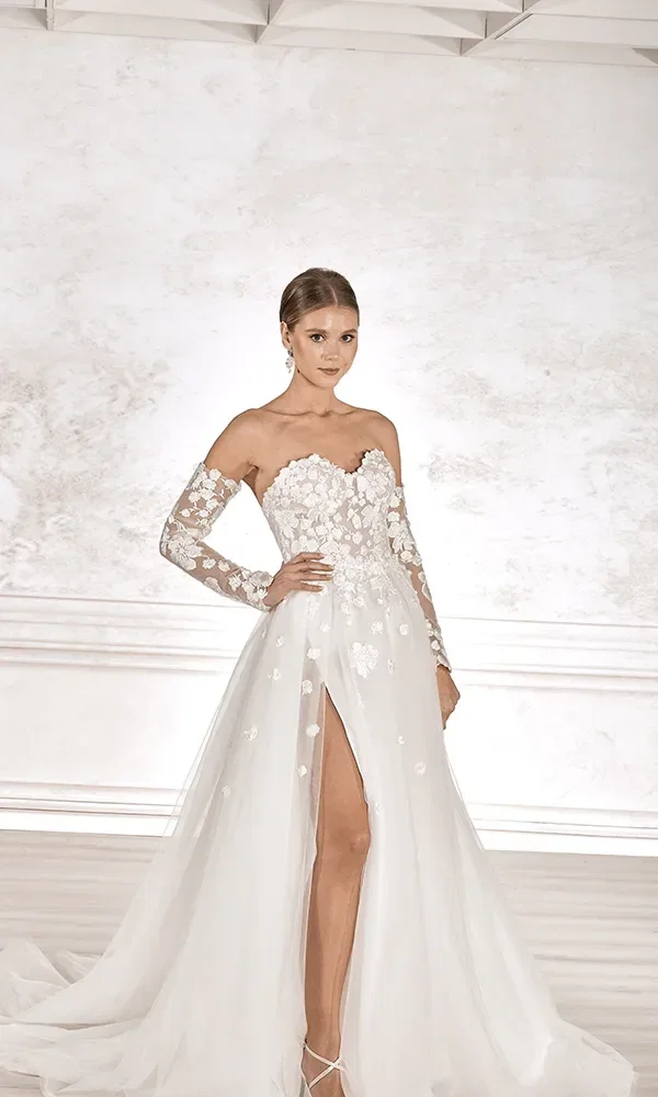 Eine Braut in einem glitzernden ärmellosen Kleid mit einem tiefen Ausschnitt und einem Schleppe aus Tüll, posiert in einem minimalistischen Raum.