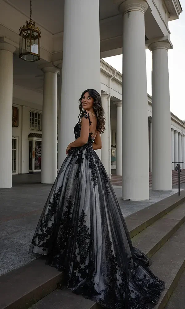 Eine Braut in einem schwarz-weißen Kleid mit Spitzenapplikationen und einer Schleppe posiert auf einer Treppe mit klassischen Säulen.
