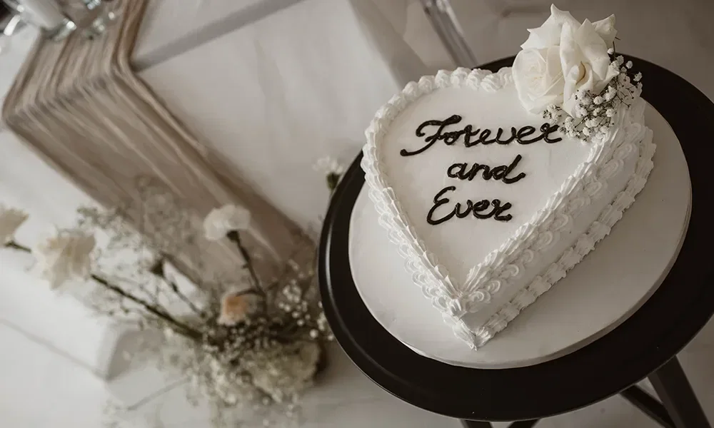 Weiße Retro-Hochzeitstorte in Herzform mit der Aufschrift 'Forever and Ever', verziert mit weißen Blumen