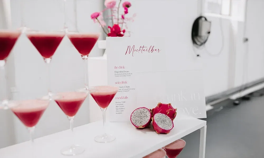 Pinkfarbene Mocktails in Martini-Gläsern, dekoriert mit Drachenfrucht, neben einer Menükarte