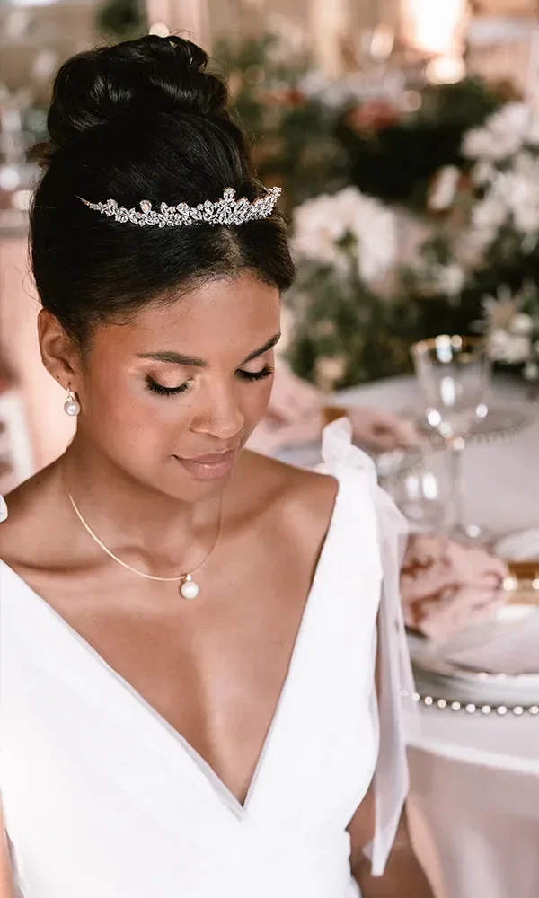 Braut mit eleganter Tiara und Perlenohrringen, die bei einer glamourösen Hochzeit sitzt