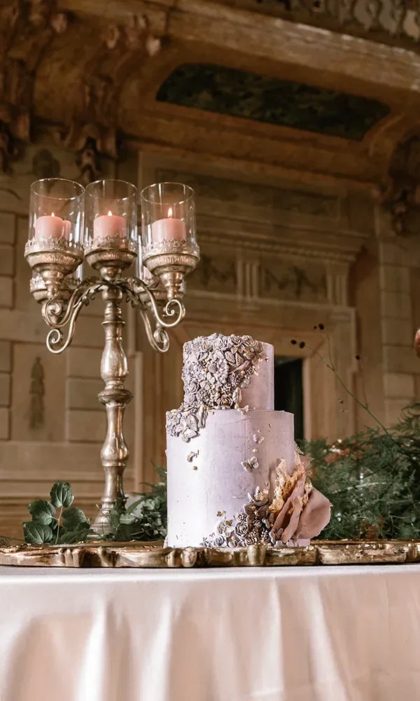 Zweistöckige Hochzeitstorte mit filigranen Verzierungen und Kerzenständern auf einem reich dekorierten Tisch