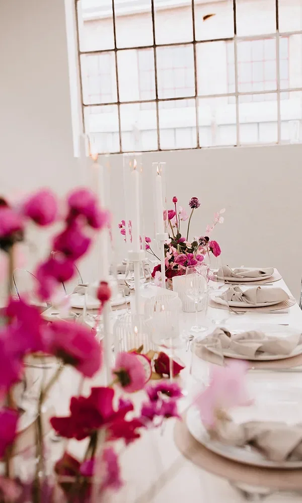 Tischdekoration mit pinken Blumen und weißen Kerzen in einem modernen, hellen Raum