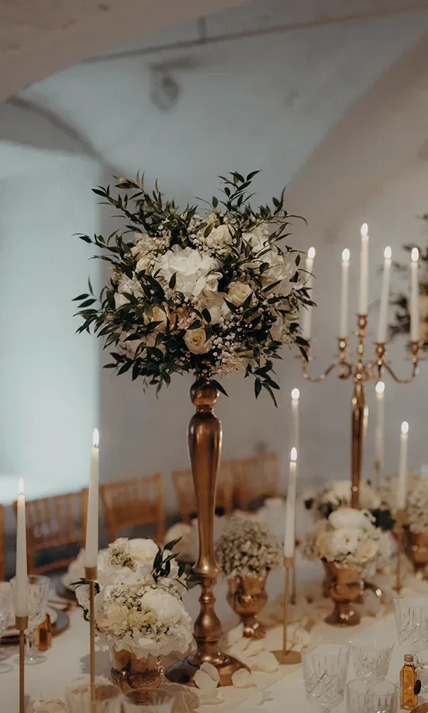 Vintage-Tischdekoration mit hohen Blumengestecken und goldenen Kerzenständern in einem eleganten Raum