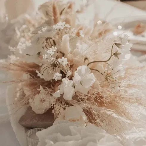 Blumengesteck mit weißen und beigen Blumen und Gräsern als Tischdekoration bei einer Strandhochzeit