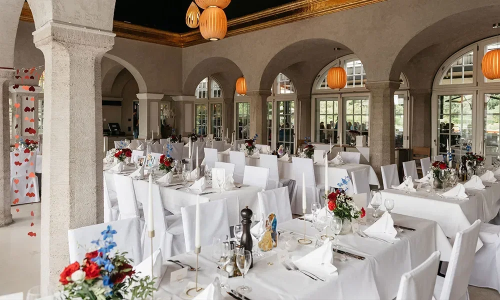 Hochzeitslocation, die Tische sind mit weißen Tischdecken bestückt und die Stühle mit weißen Hussen.
