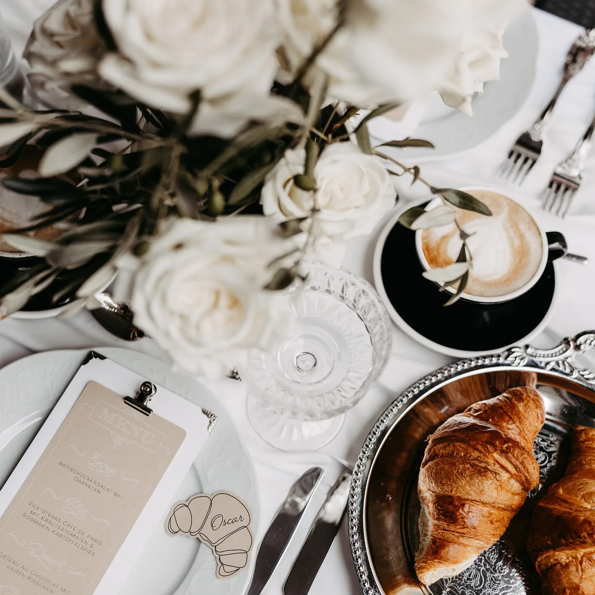 Ein gedeckter Tisch mit weißen Blumen, Kaffee und Croissant