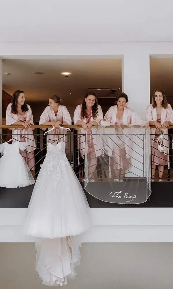 Team Bridal posiert auf einem Balkon, an dem das Brautkleid hängt. Brautkleid