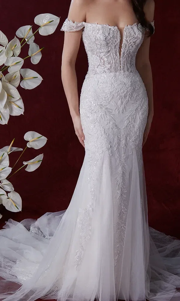 Nahaufnahme eines trägerlosen Hochzeitskleides mit einem tiefen Ausschnitt und aufwendigen Spitzenapplikationen. Der Hintergrund ist tiefrot und von weißen Blumen gesäumt.