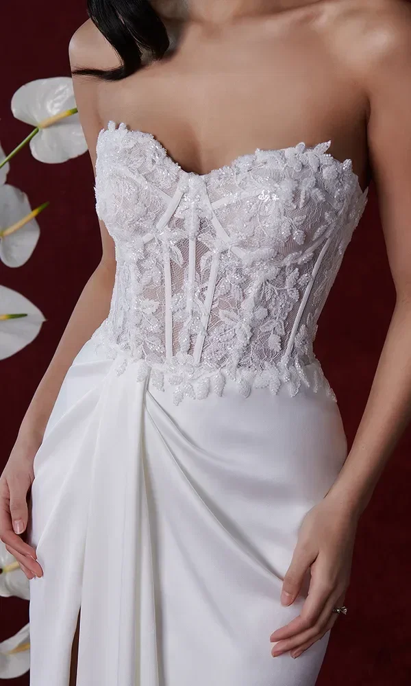 Nahaufnahme eines Korsett-Hochzeitskleides mit floralen Spitzenapplikationen. Der Hintergrund ist tiefrot und mit weißen Blumen dekoriert.