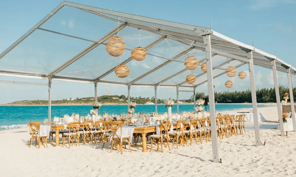 Fesrtlich geschmückte Tafel für Hochzeitsgäste direkt am Strand unter einem Glasdach.