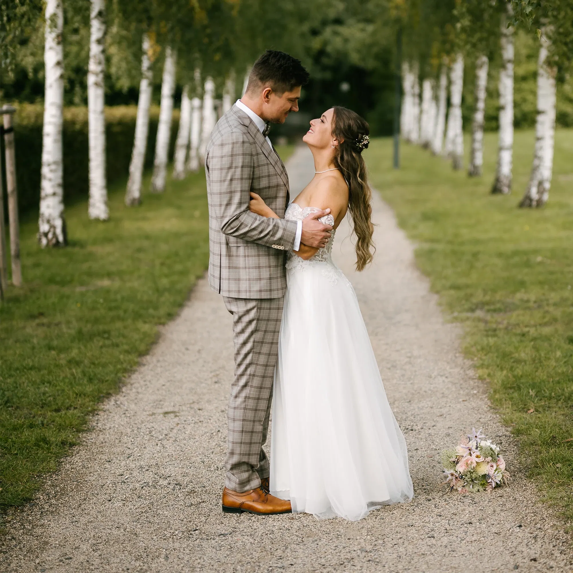 Brautpaar steht an einer Birkenallee.