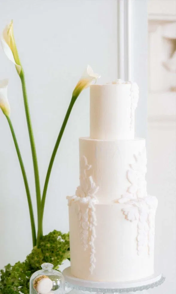 Elegante mehrstöckige Hochzeitstorte in Weiß mit floralen Details und Calla-Lilien als Dekoration.