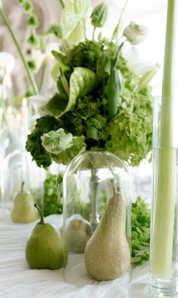 Elegante Hochzeits-Tischdekoration mit grünen Blüten, Callas, Kerzen in Glasvasen und Birnen unter Glasglocken.