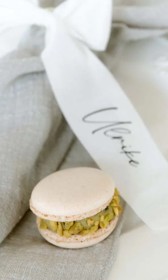 Zarter Pistazien-Macaron als Hochzeitsgastgeschenk auf Leinenstoff mit personalisiertem Seidenband.