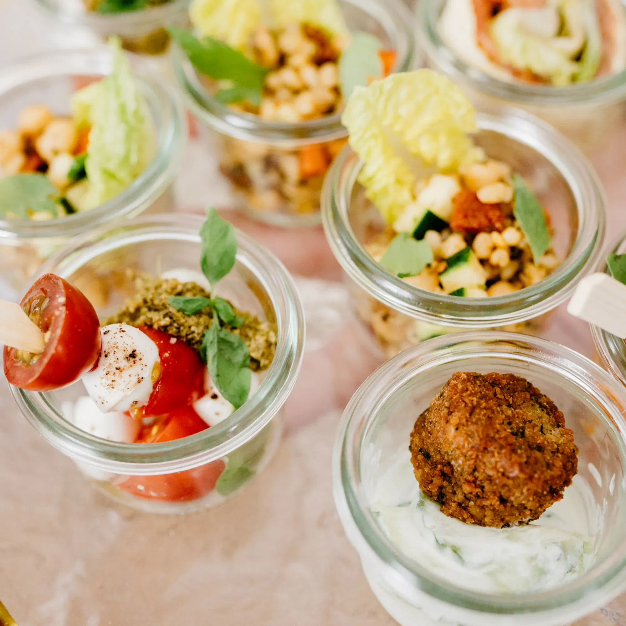 Kleine Glasgefäße mit verschiedenen mediterranen Vorspeisen, darunter Caprese-Salat und Falafel mit Joghurtdip, elegant angerichtet.