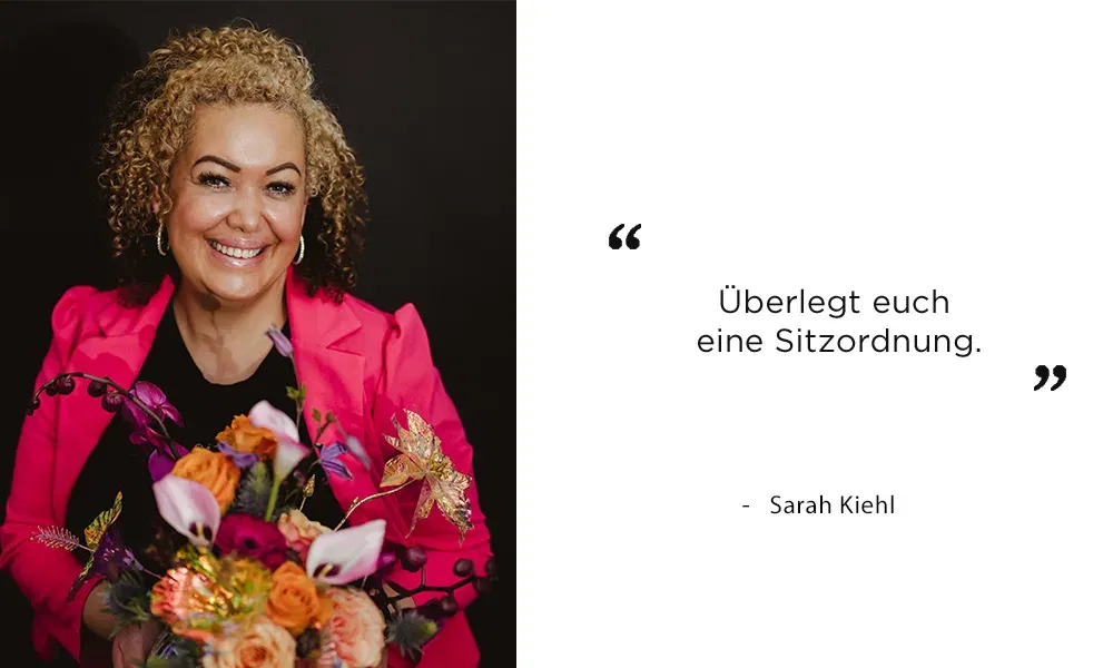 Sarah Kiehl in einem pinken Blazer, die einen Blumenstrauß hält und wertvolle Hochzeitsplanungstipps gibt.