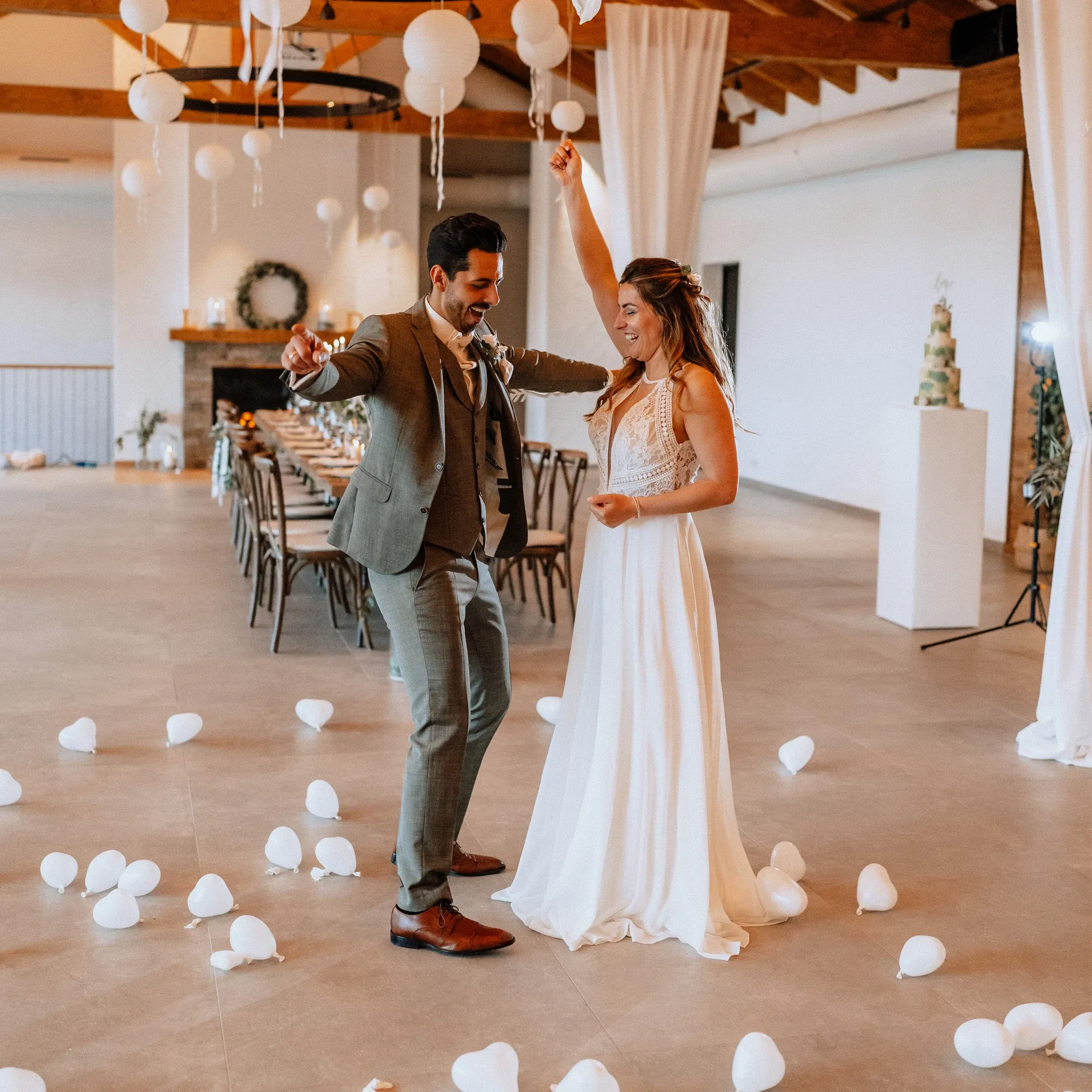 Brautpaar tanzt in einer festlich dekorierten Hochzeitslocation mit hängenden weißen Papierlaternen und verstreuten weißen Luftballons, während es den Moment genießt.