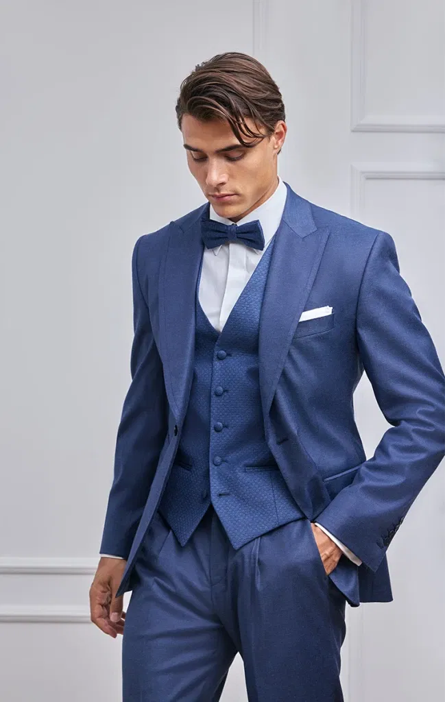 Detailaufnahme eines Bräutigams im dunkelblauen Hochzeitsanzug mit strukturierter Weste und Fliege.
