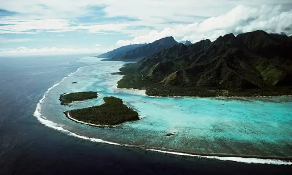 Küstenlinie mit Lagune und vorgelagerten Inseln, eingerahmt von dunklen Berghängen und türkisblauem Meerwasser.