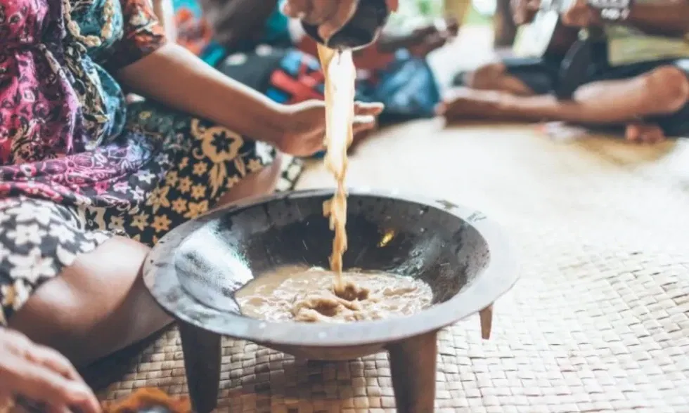 Kulturelles Ritual: Flüssigkeit wird aus einem Tuch in eine runde Schale gepresst, während andere Teilnehmer im Hintergrund sitzen.