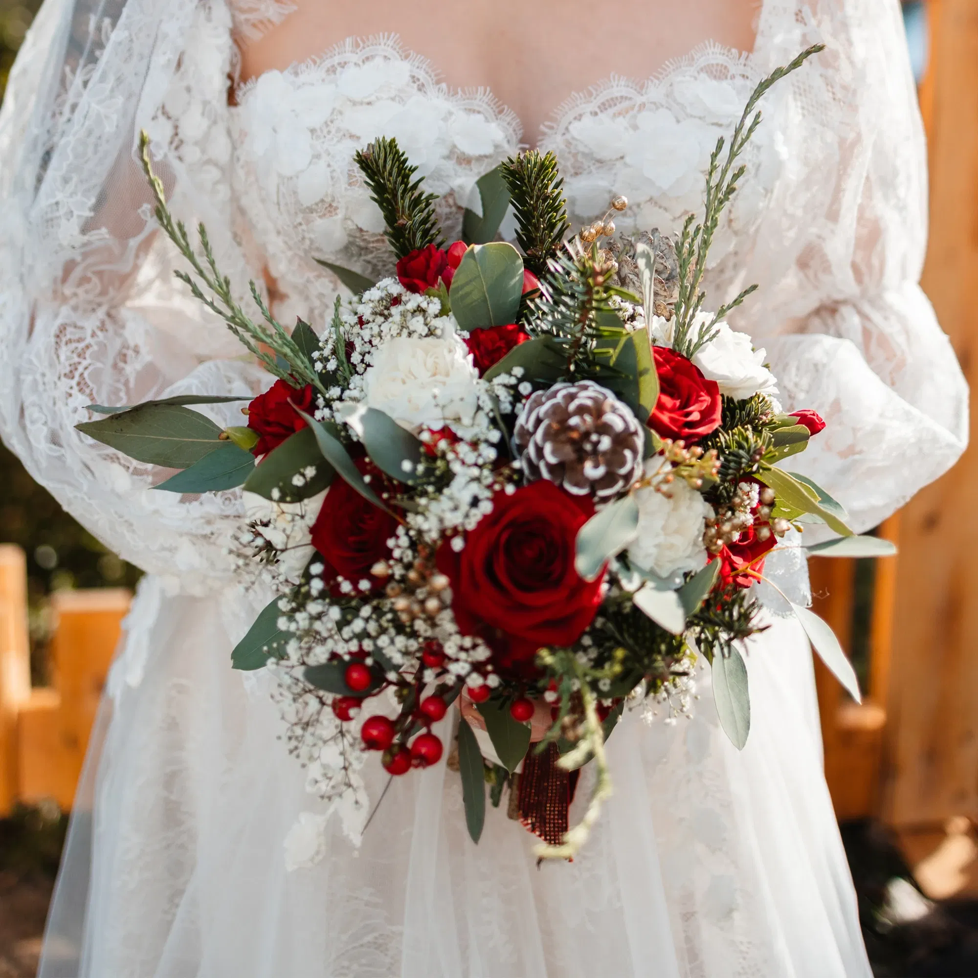 Romantischer Brautstrauß mit roten und weißen Rosen, Tannenzweigen, Eukalyptus, Beeren und einer dekorativen Zapfenverzierung, passend zur Winterhochzeit.