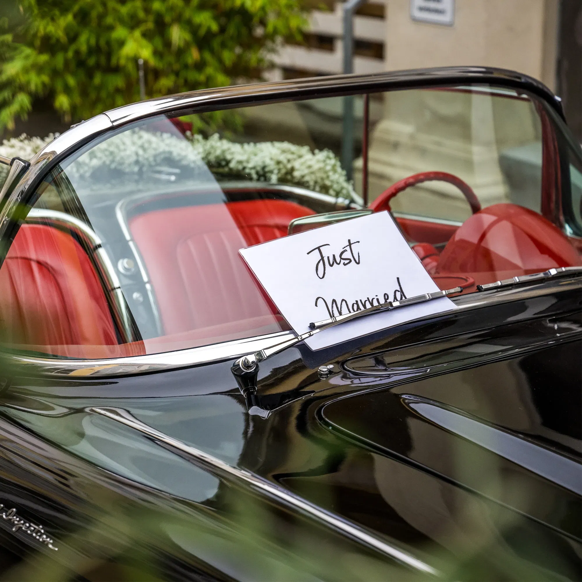 Schwarzes Cabrio mit rotem Innenraum und einem ‚Just Married‘-Schild auf der Windschutzscheibe, dekoriert für eine Hochzeit.