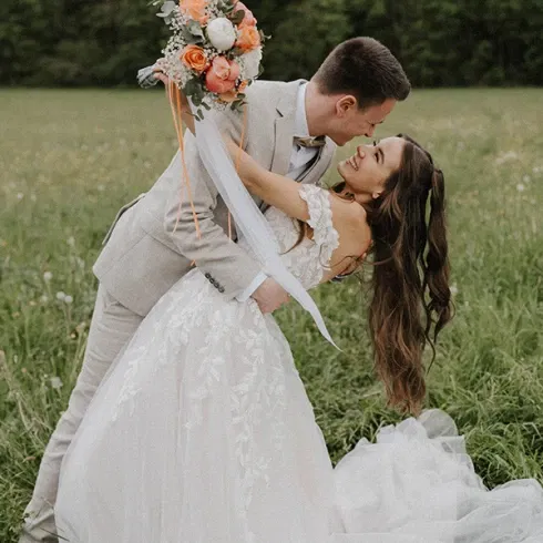 Braut und Bräutigam in einer romantischen Pose auf einer grünen Wiese, Braut in einem Spitzenkleid mit langem Schleier.