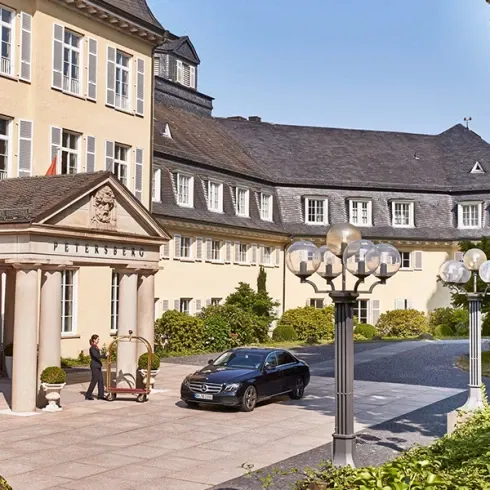 Außenansicht des Grandhotels Petersberg mit klassischer Architektur, einem gepflegten Eingangsbereich und einem geparkten Auto.
