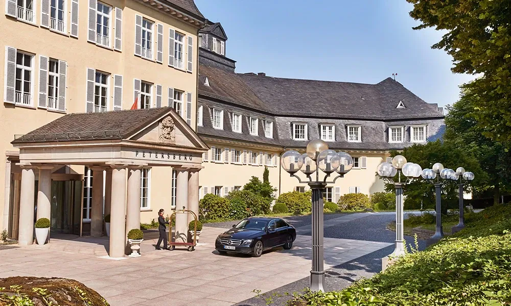 Außenansicht des Grandhotels Petersberg mit klassischer Architektur, einem gepflegten Eingangsbereich und einem geparkten Auto.