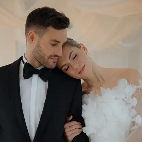 Braut und Bräutigam in eleganter Hochzeitskleidung, die Braut lehnt ihren Kopf sanft an die Schulter des Bräutigams, während sie gemeinsam einen ruhigen Moment genießen.