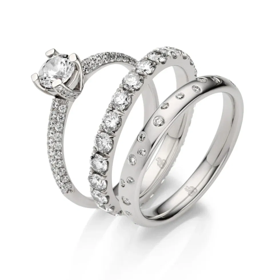 Drei funkelnde Ringe in Weißgold: Verlobungsring mit Solitär, Memoire-Ring mit großen Diamanten und zarter Ehering mit Pavé-Fassung.