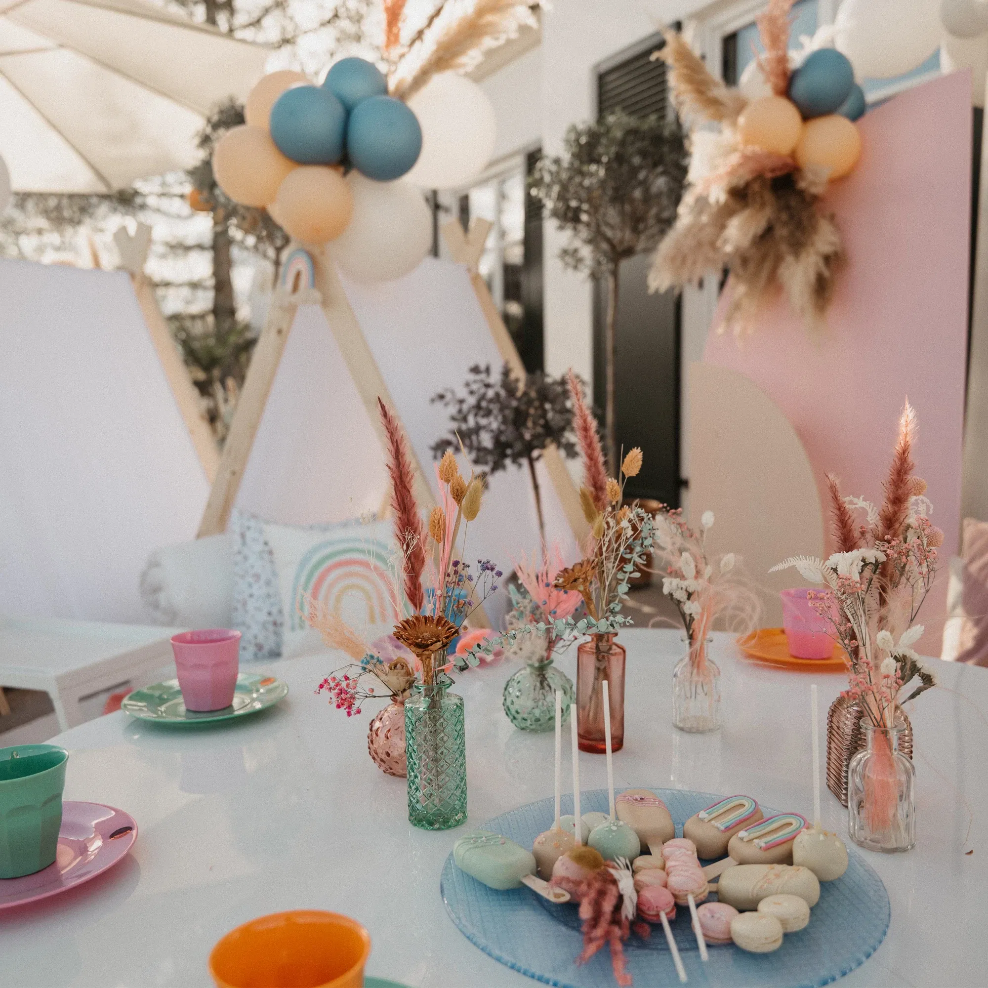 Farbenfrohe Tischdekoration für eine Gartenparty mit Boho-Elementen, Trockenblumen und bunten Tellern, ideal für Kinder oder sommerliche Feiern.