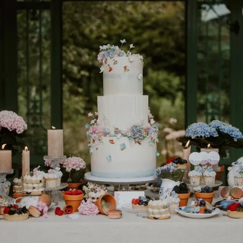 Elegante Hochzeitstorte mit floralem Design, umgeben von Hortensien und Kerzen, perfekt präsentiert auf einem dekorativen Sweet Table.