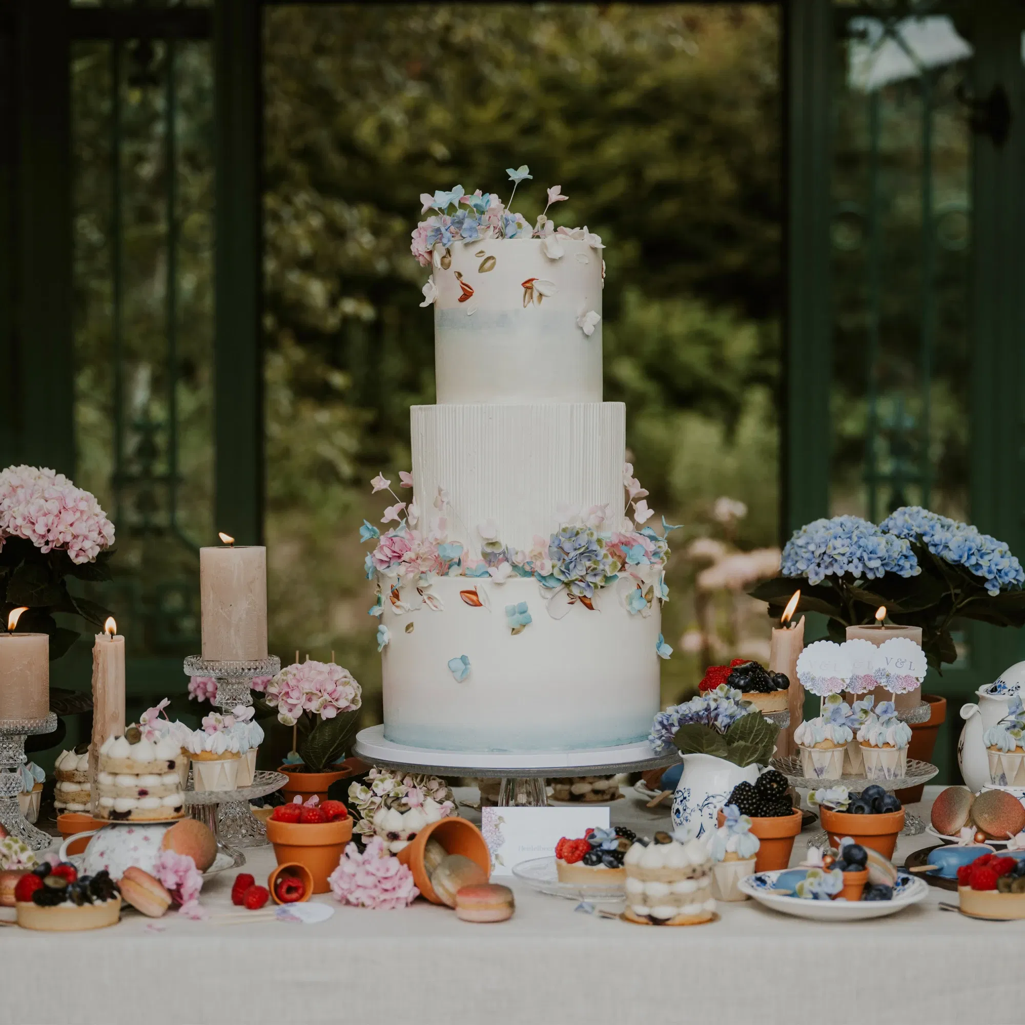 Elegante Hochzeitstorte mit floralem Design, umgeben von Hortensien und Kerzen, perfekt präsentiert auf einem dekorativen Sweet Table.