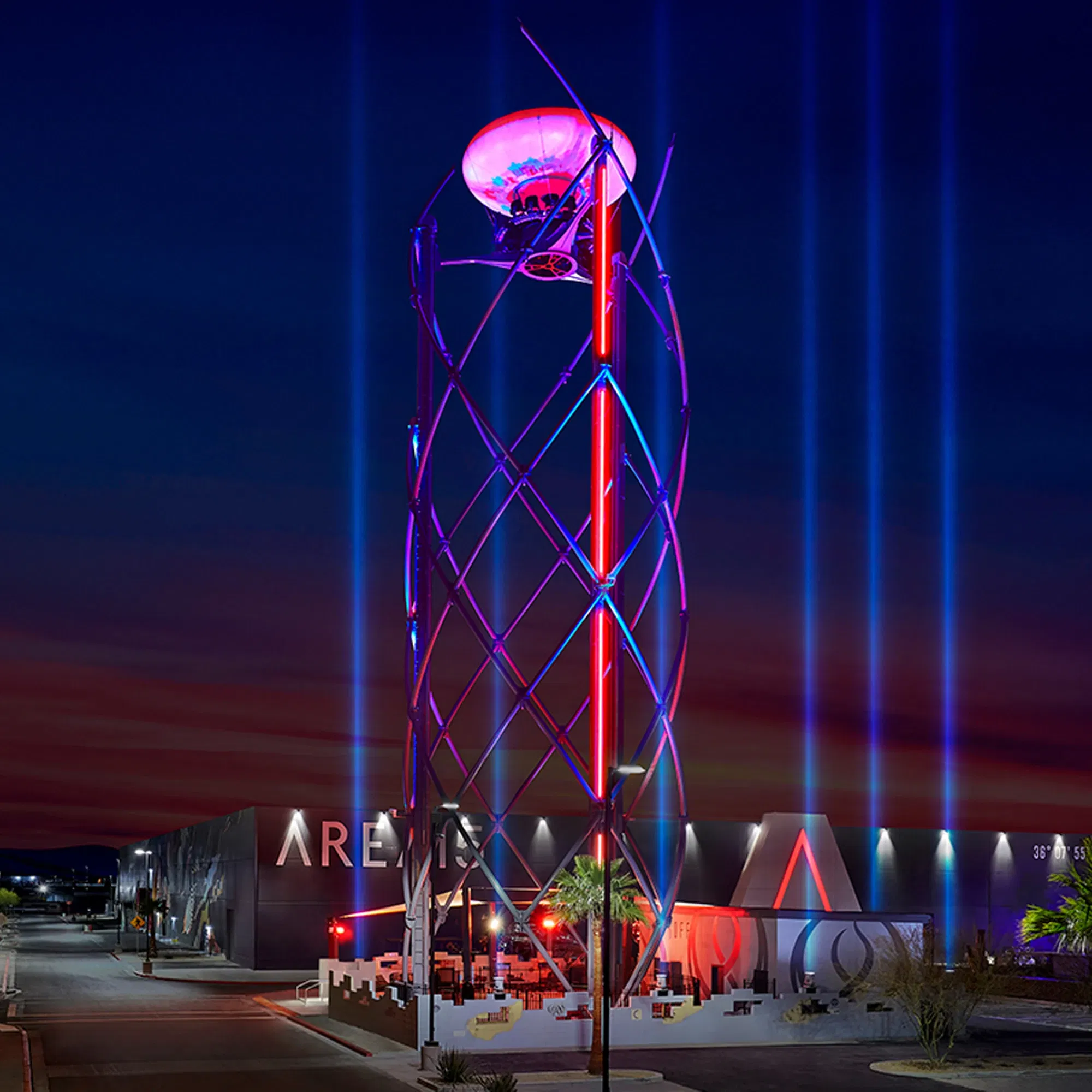 Moderne Installation der AREA15 mit leuchtenden Lichtern und einer futuristischen Struktur bei Nacht, aufgenommen vor einem farbenfrohen Himmel.