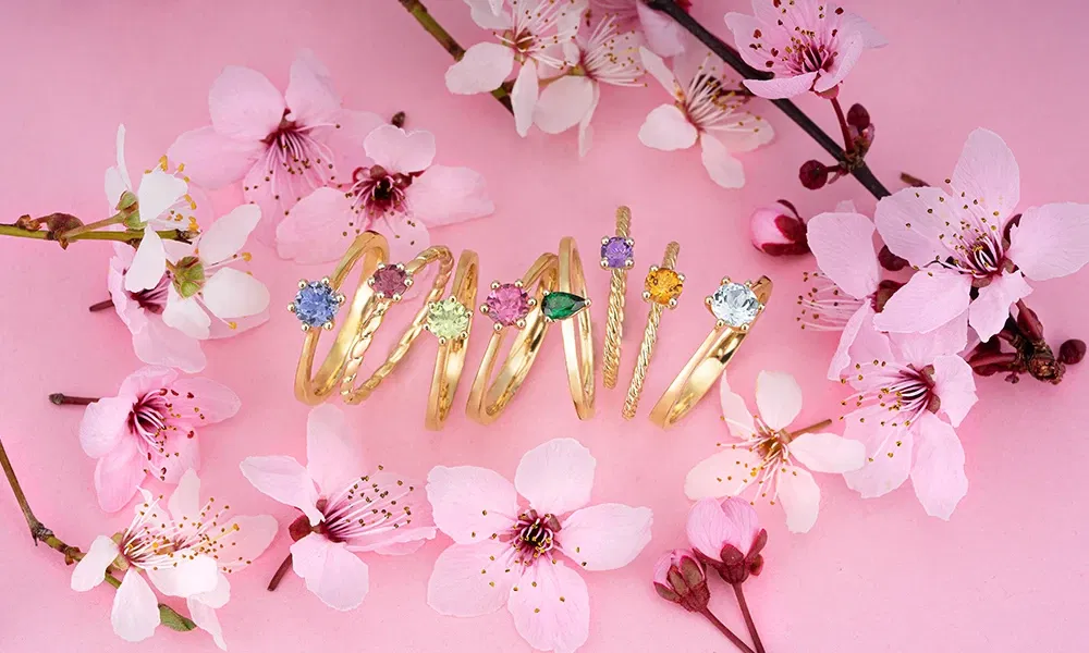 Goldene Ringe mit farbigen Edelsteinen, eingerahmt von rosa Kirschblüten
