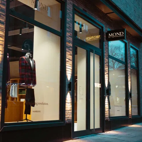 Beleuchtetes Schaufenster eines Herrenausstatters mit elegantem Anzug auf einer Schneiderpuppe und moderner Glasfassade in der Abenddämmerung