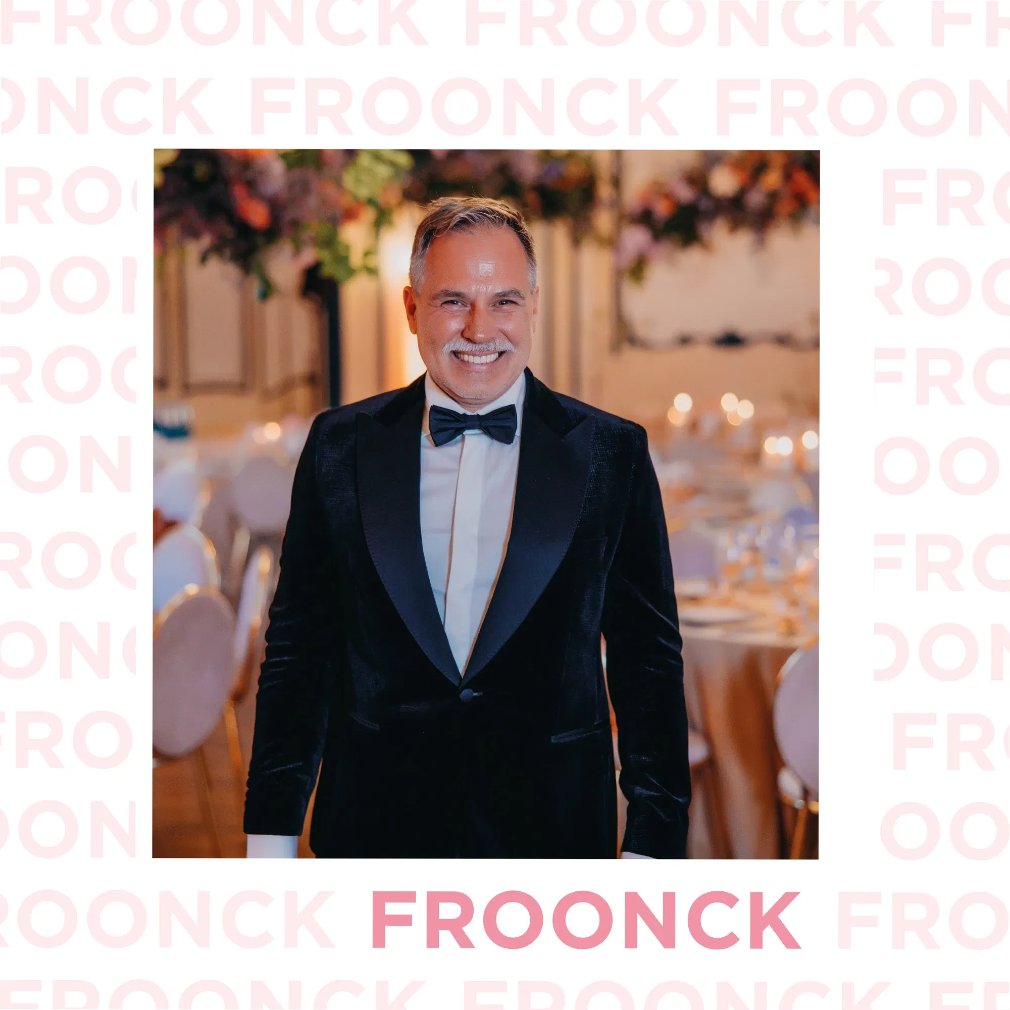 Hochzeitsplaner Froonck strahlt in elegantem Smoking vor einer festlich dekorierten Hochzeitslocation mit warmem Kerzenlicht und Blumenarrangements.