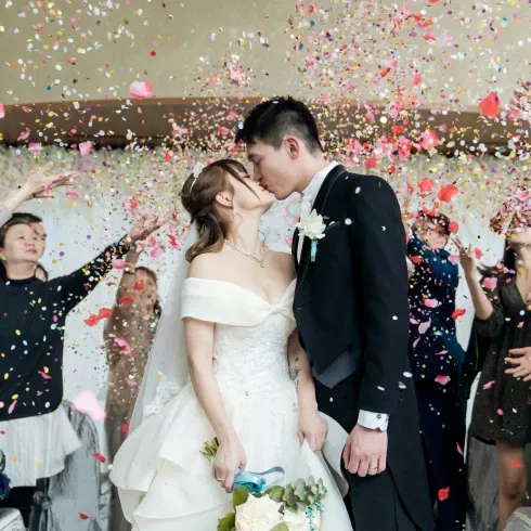 Brautpaar küsst sich unter einem Konfettiregen, umgeben von jubelnden Hochzeitsgästen in festlicher Stimmung.