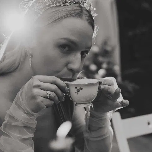 Schwarz-weißes Hochzeitsfoto einer Braut mit Diadem, die während der Feier aus einer feinen Teetasse trinkt.