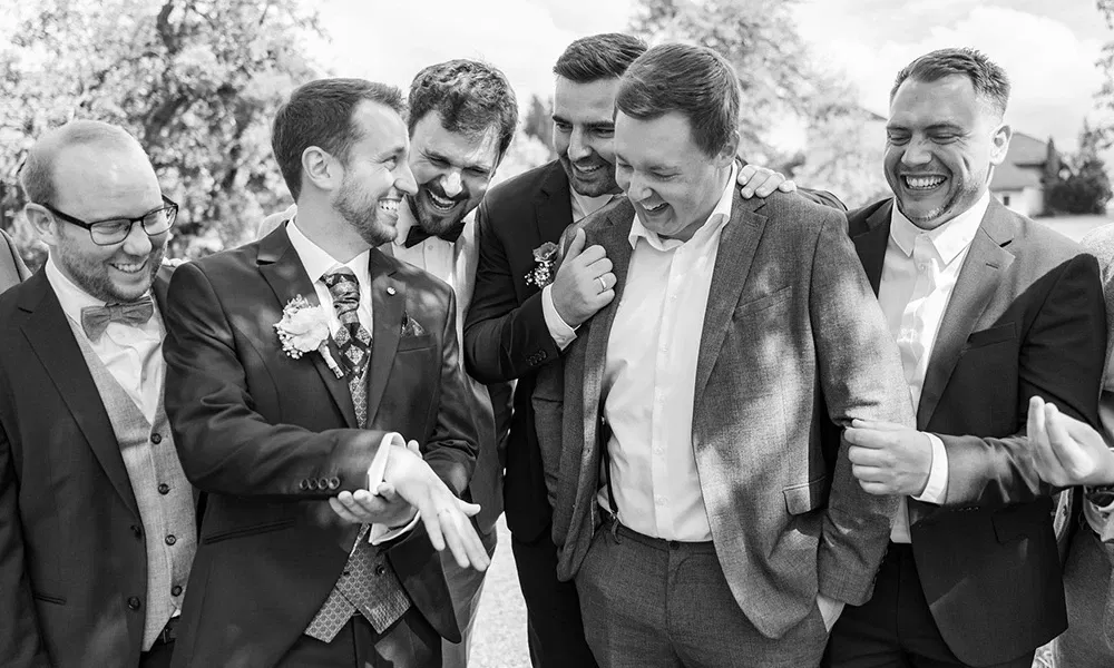 Schwarz-weiß Foto: Bräutigam lacht mit seinen Trauzeugen in gelöster Stimmung.
