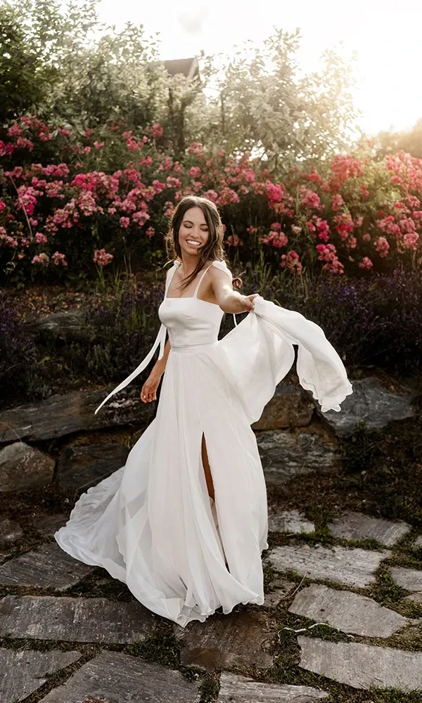 Fröhliche Braut schwingt ihr Kleid im Garten voller bunter Blumen.