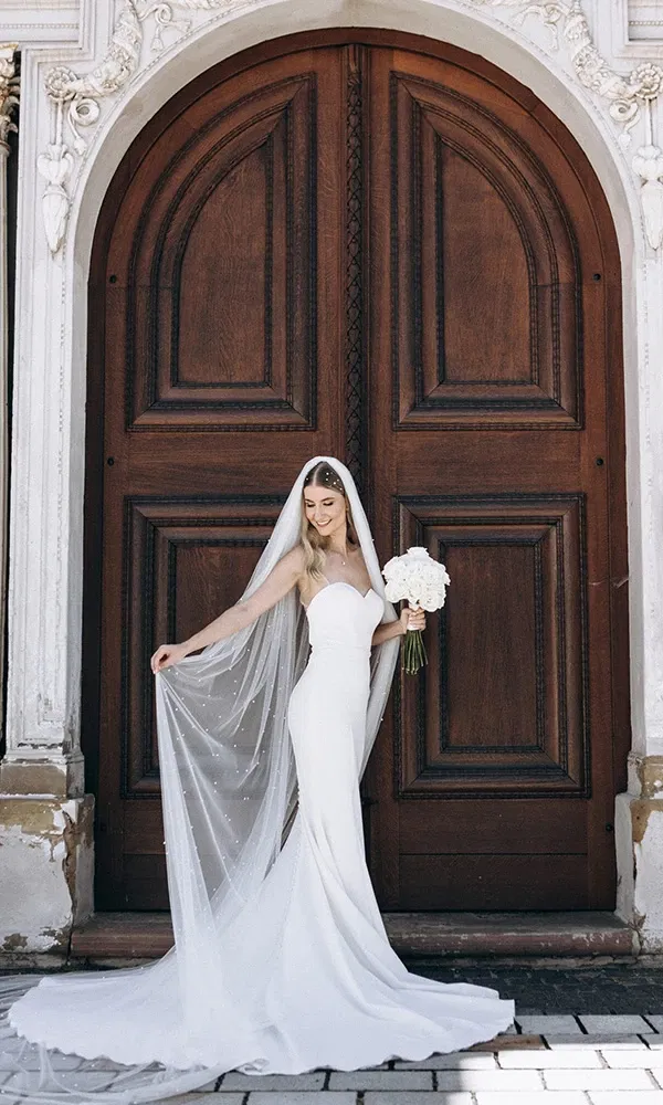 Klassische Braut mit langem Schleier vor antikem Holztor.