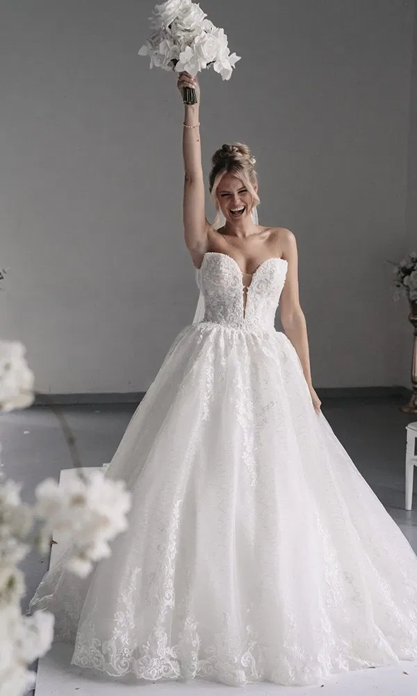 Braut hebt lachend den Blumenstrauß in einem hellen Atelier.