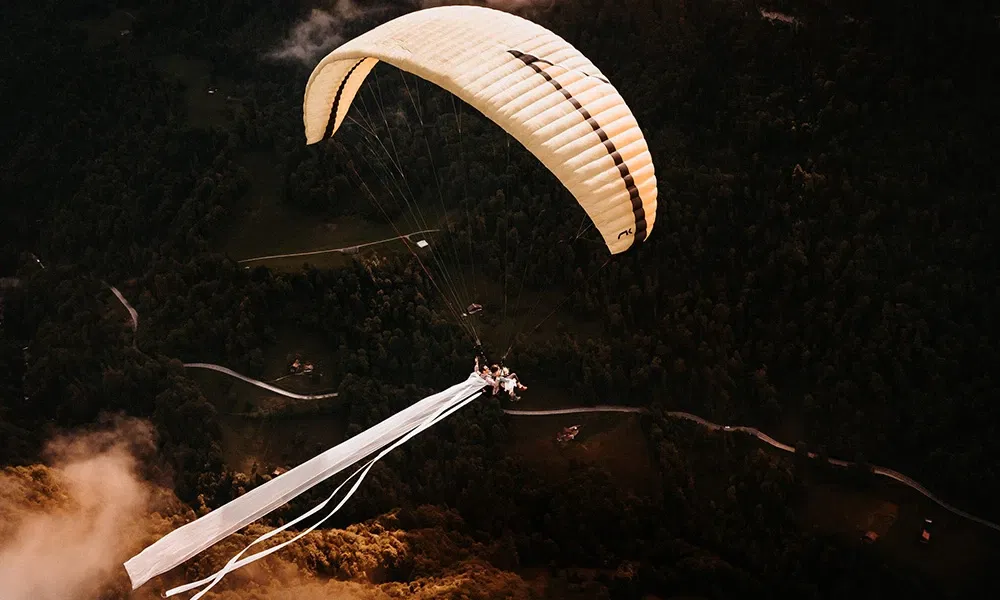 Abenteuerliches Brautpaar fliegt mit Gleitschirm über eine beeindruckende Berglandschaft.