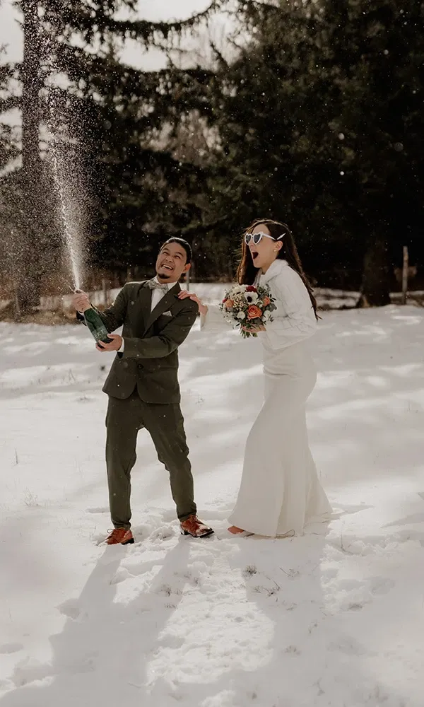 Winterhochzeit mit viel Spaß: Bräutigam spritzt Champagner, Braut lacht überrascht.
