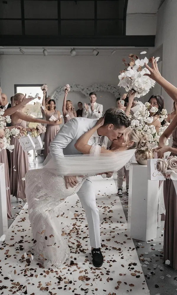 Brautpaar küsst sich leidenschaftlich nach der Trauung unter jubelnden Gästen.