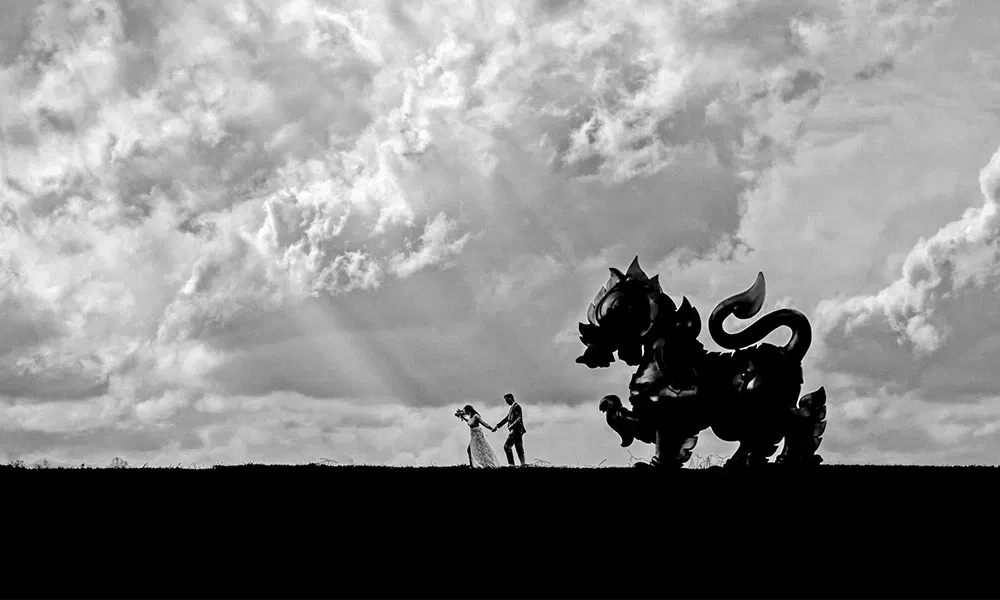 Künstlerische Schwarzweißaufnahme eines Brautpaars mit mythischer Statue im Hintergrund.